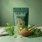 Aarogya Nutri Mix Moringa Powder pouch next to a wooden spoon filled with green moringa powder and fresh leaves.