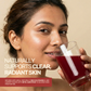 A close-up of a woman with radiant skin holding a glass of healthy red wellness juice for skin nourishment.
